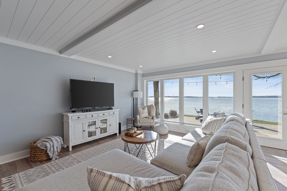 Family room with white sectional, TV and lake-view windows under a beamed ceiling