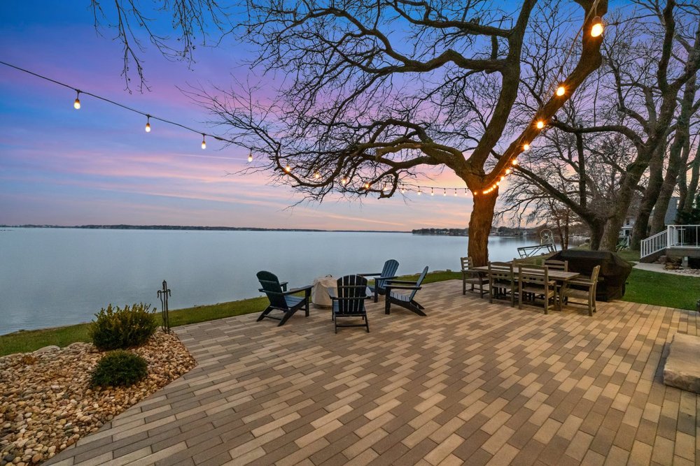 Lakefront patio at dusk with string lights and fire pit seating